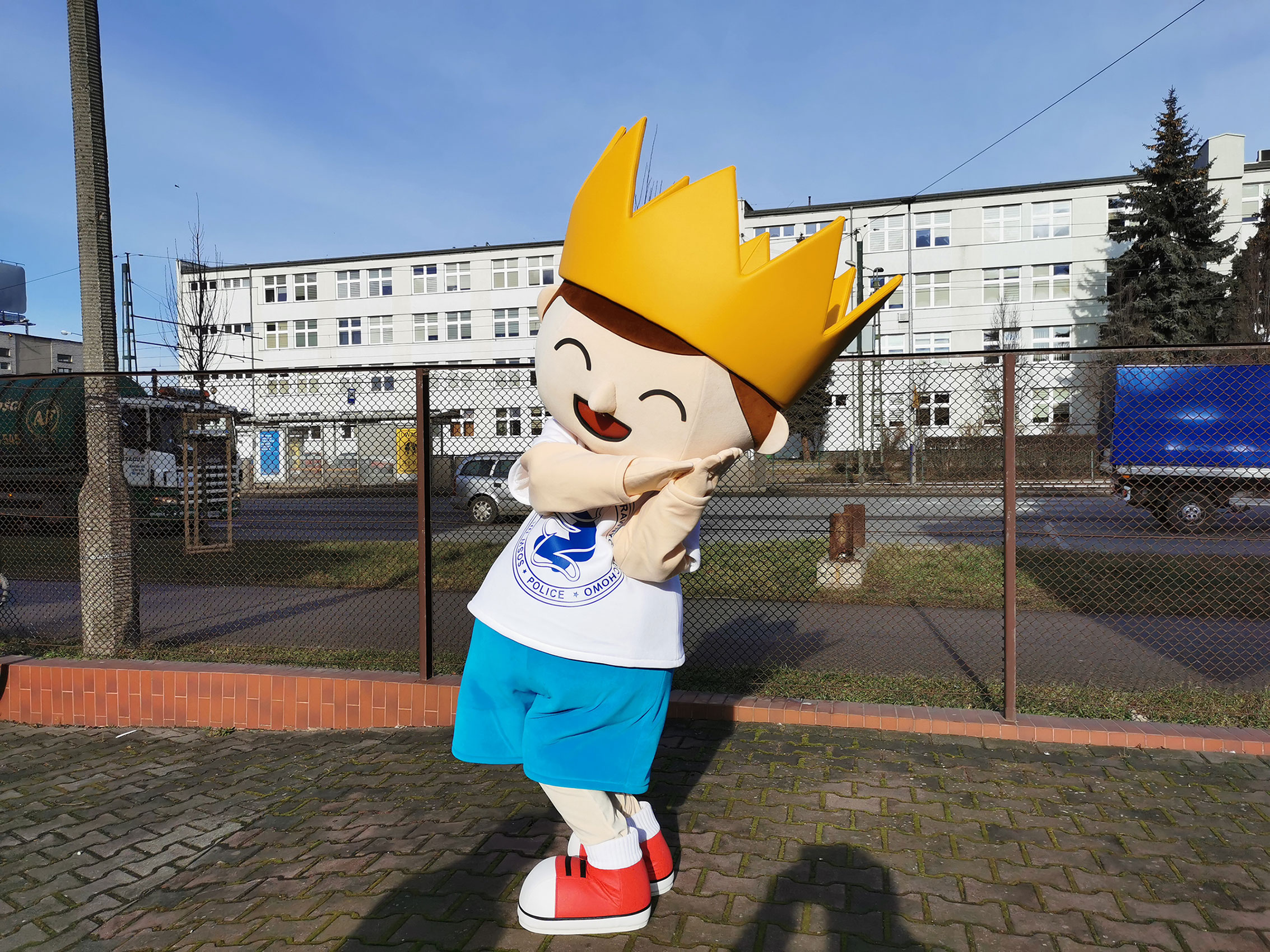 Na fotografii widnieje maskotka w postaci króla pozująca do zdjęcia obok siedziby firmy Elabika